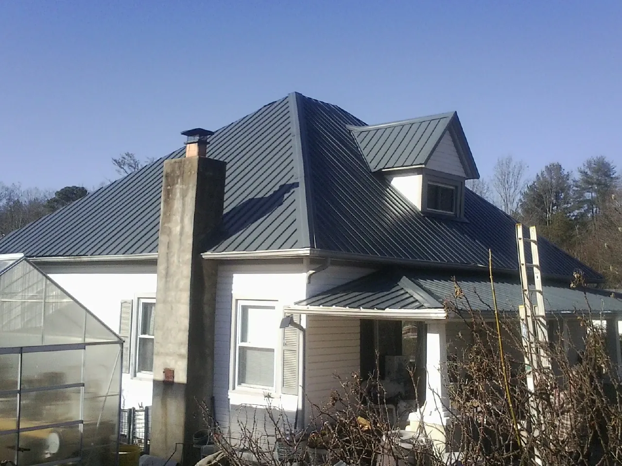 Dark blue standing seam metal roof on a white farmhouse with dormer — Slate & Tile Roof Repair by Roofing Brothers in Blakeslee