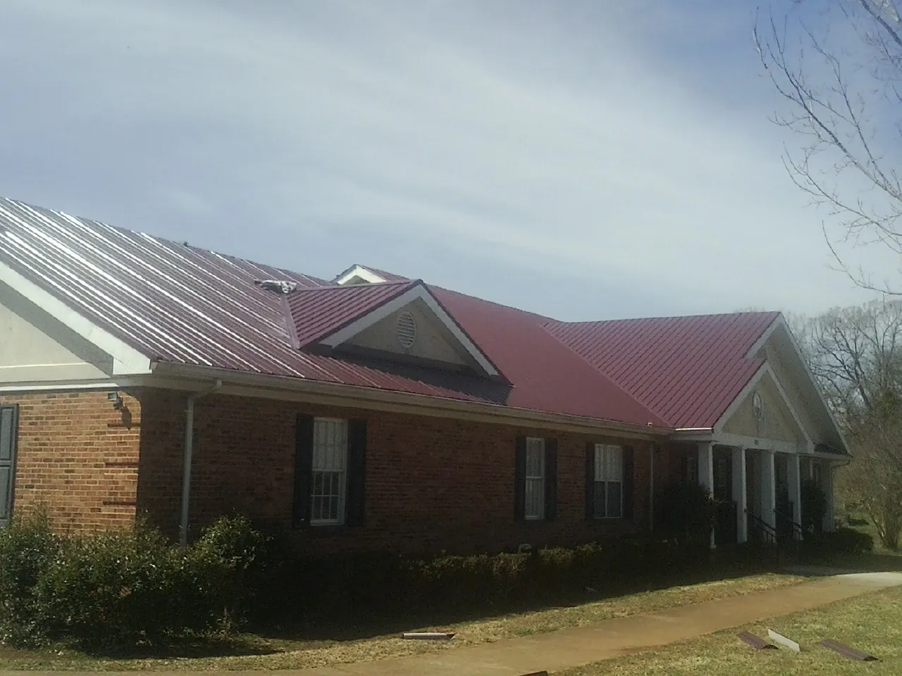 Red metal roof with gabled entries on a long brick building, from a Hail Damage Roof Repair job in Blakeslee