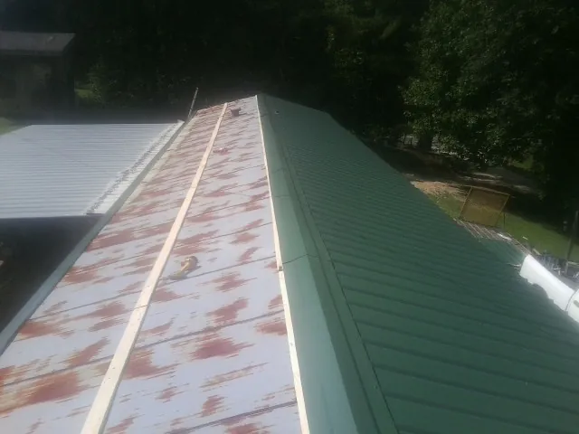 Old rusted panels beside newly installed green metal roofing — Wind Damage Roof Repair by Roofing Brothers in Blakeslee