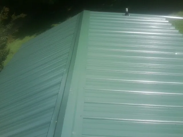 New green metal panels meeting at the ridge of a roof — Flat Roof Repair work by our crew in Blakeslee