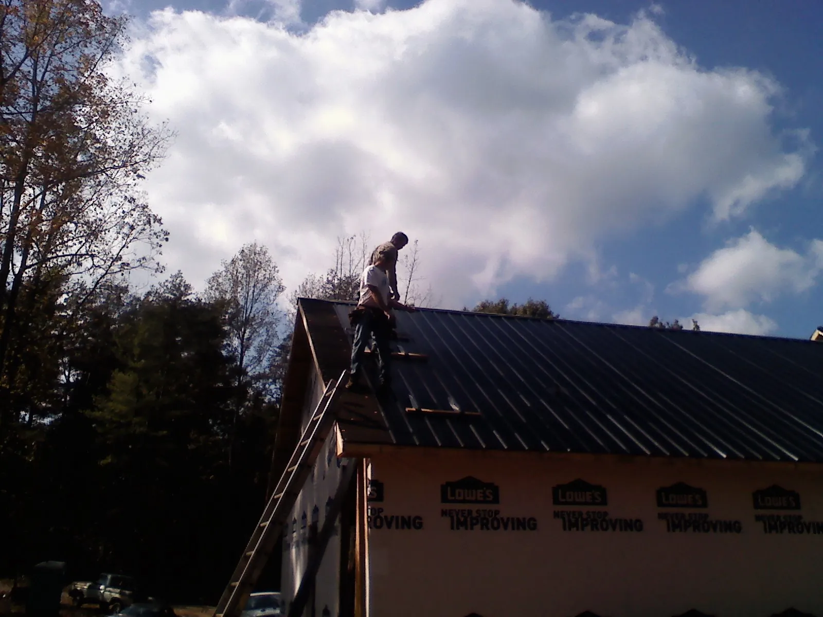 Roofer fastening dark metal panels high against a cloudy sky, from a Roof Inspection job in Blakeslee
