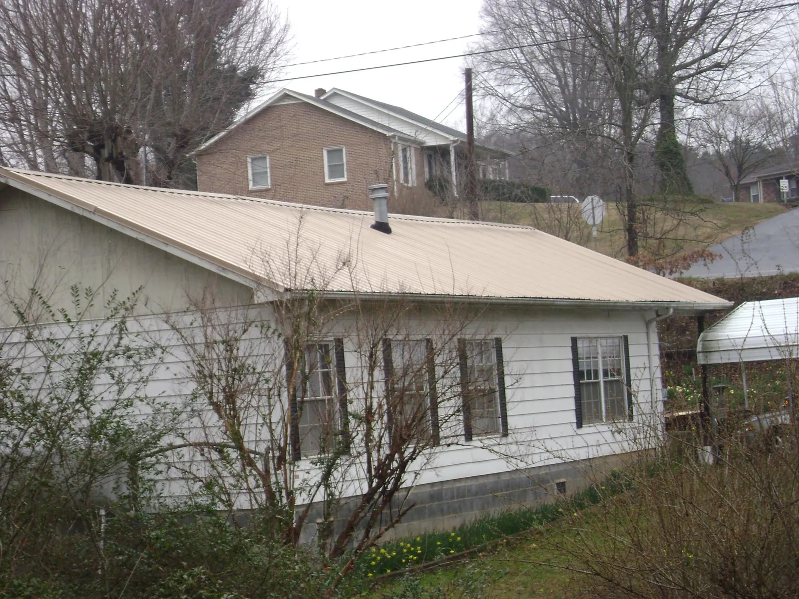 Tan metal roof on a white sided house set into a hillside — Commercial Roofing by Roofing Brothers in Blakeslee