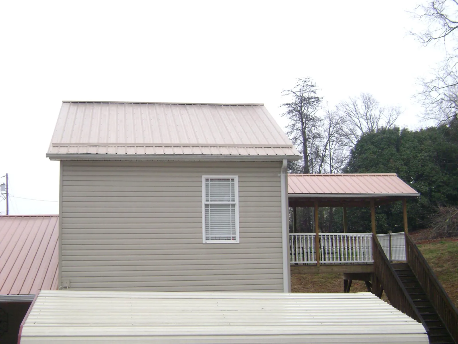 Tan metal roofs on a two story addition and attached porch, from a Roof Replacement job in Blakeslee